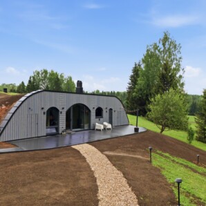 Revonia underground house exterior side view – arched earth-sheltered modular home with garden terrace and chairs in Estonian countryside