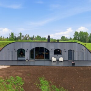 Revonia underground house exterior – completed earth-sheltered modular home with arched metal roof and garden terrace at Riverberg estate, Otepää